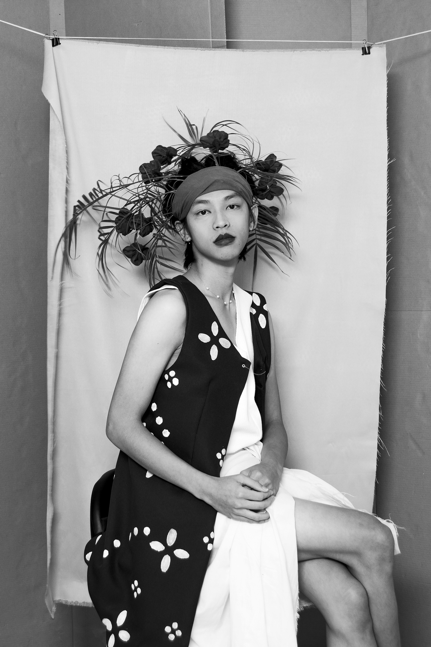 a seated figure photographed in black and white. They are wearing a headband with ferns and roses coming out of it.