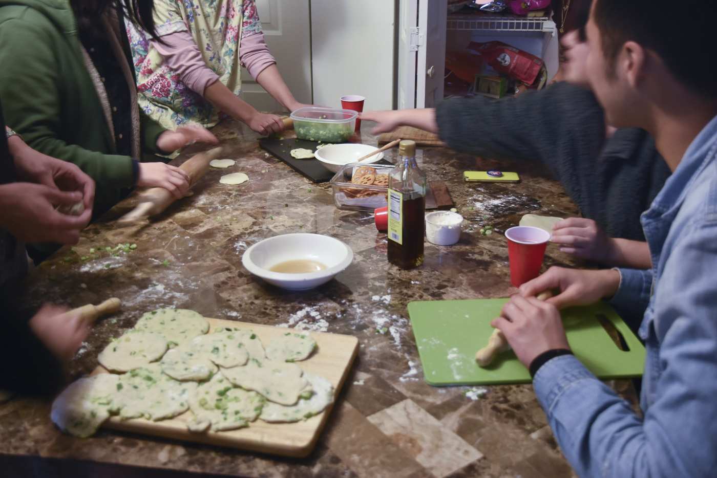 various people gathered rolling out dough to cook scallion pancakes
