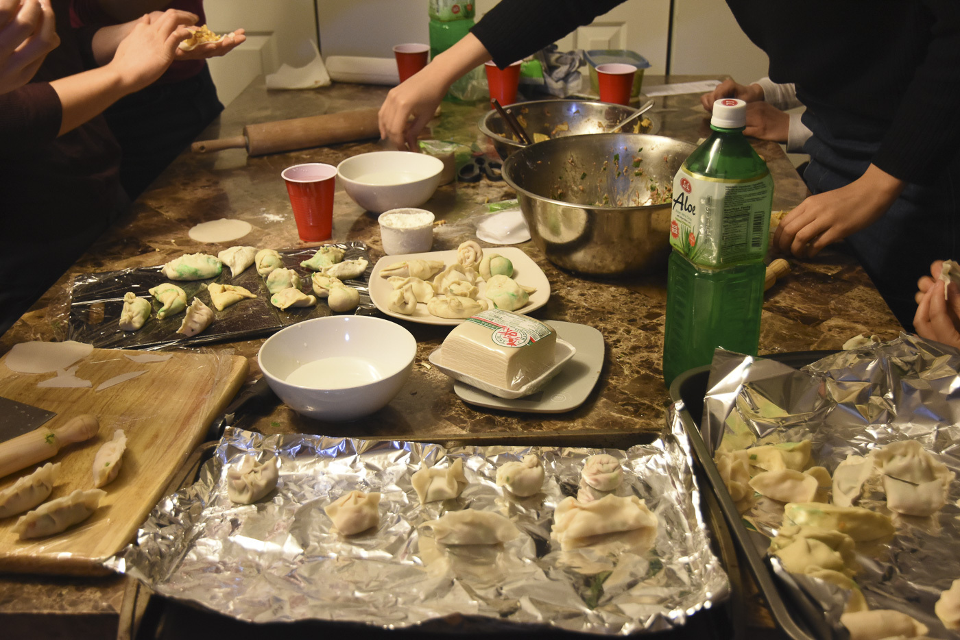 various people gathered around a table rolling, wrapping, and making dumplings