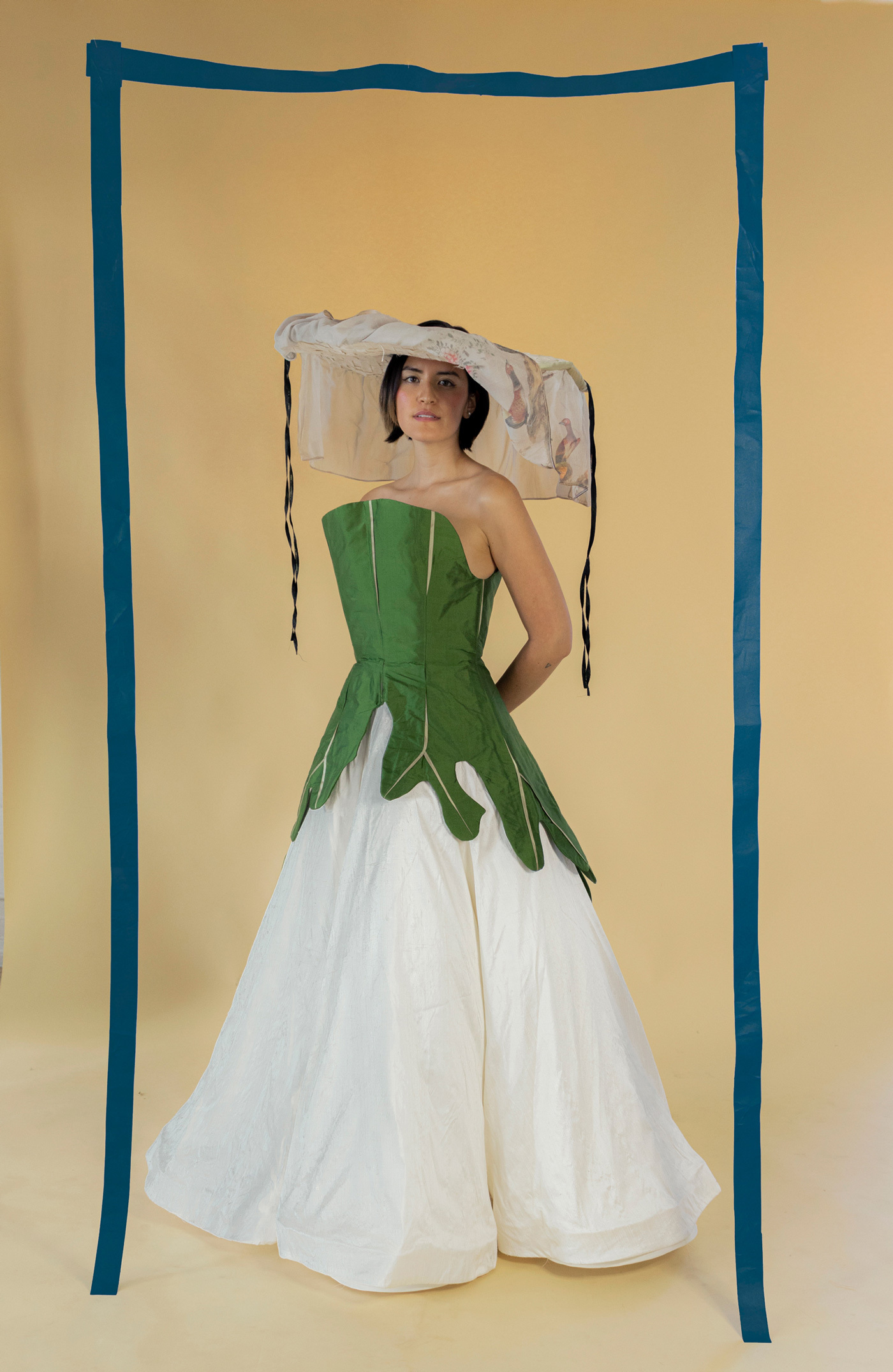 Crystal stands wearing a leaf inspired green and white dress. She is framed with hanging blue tape