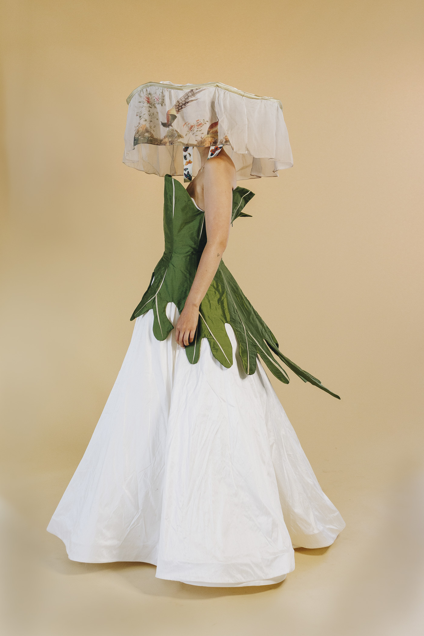 Crystal stands facing to the left wearing a Hakka-style hat and a large leaf-inspired dress