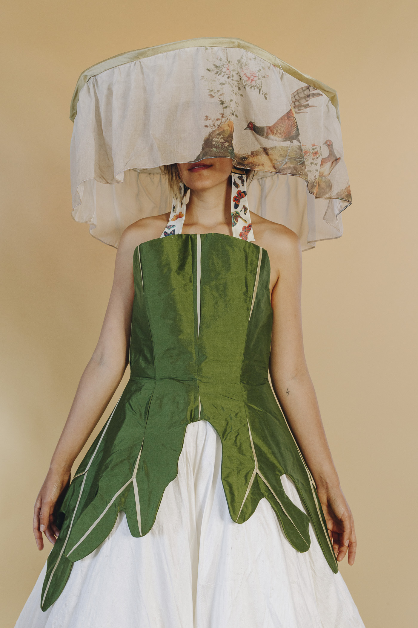 An image of Crystal from the thigh up wearing a large white and green gown and a veiled headpiece