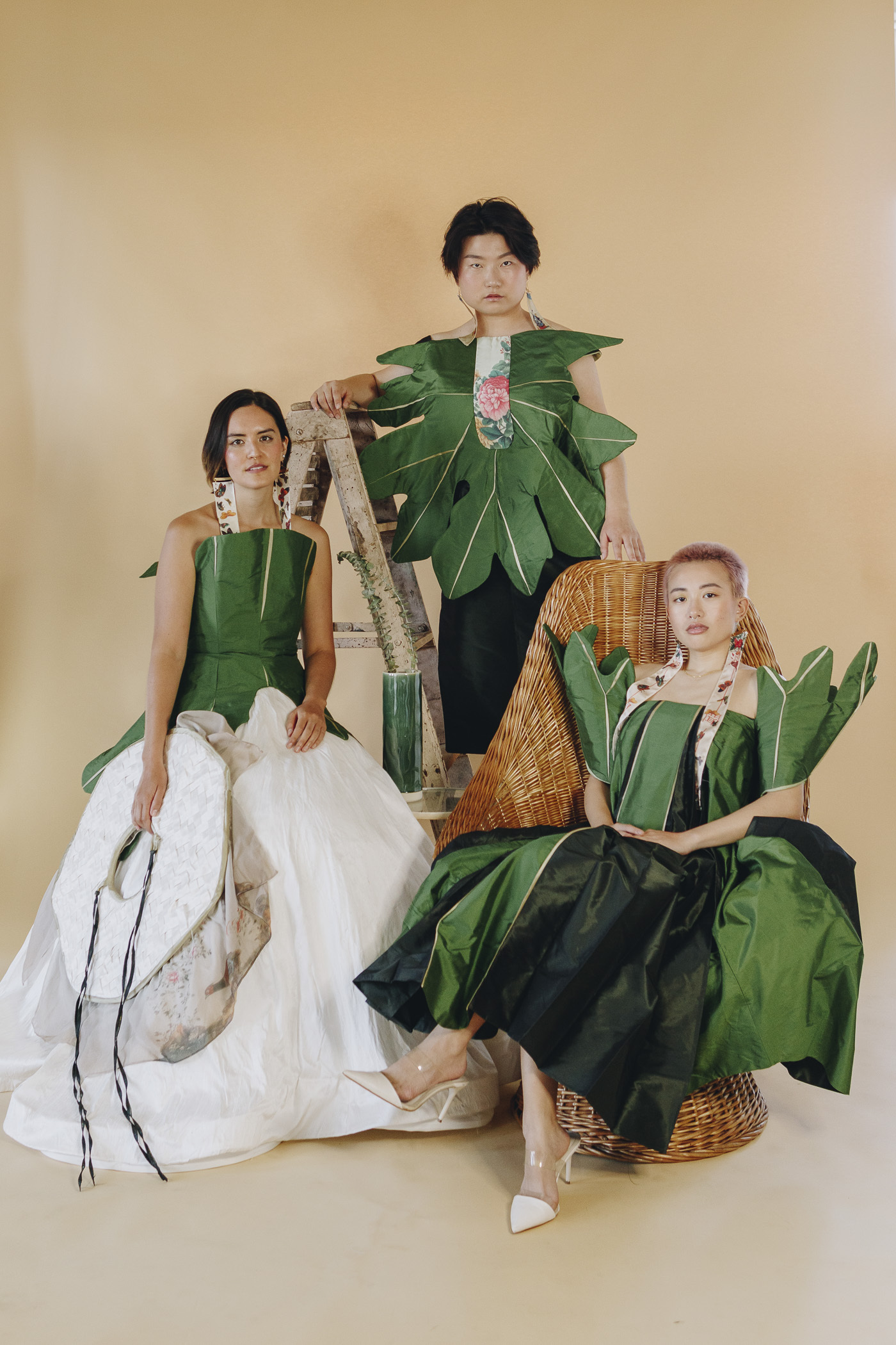 Three individuals wearing large green tetrapanax papyrifer leaf-inspired dresses