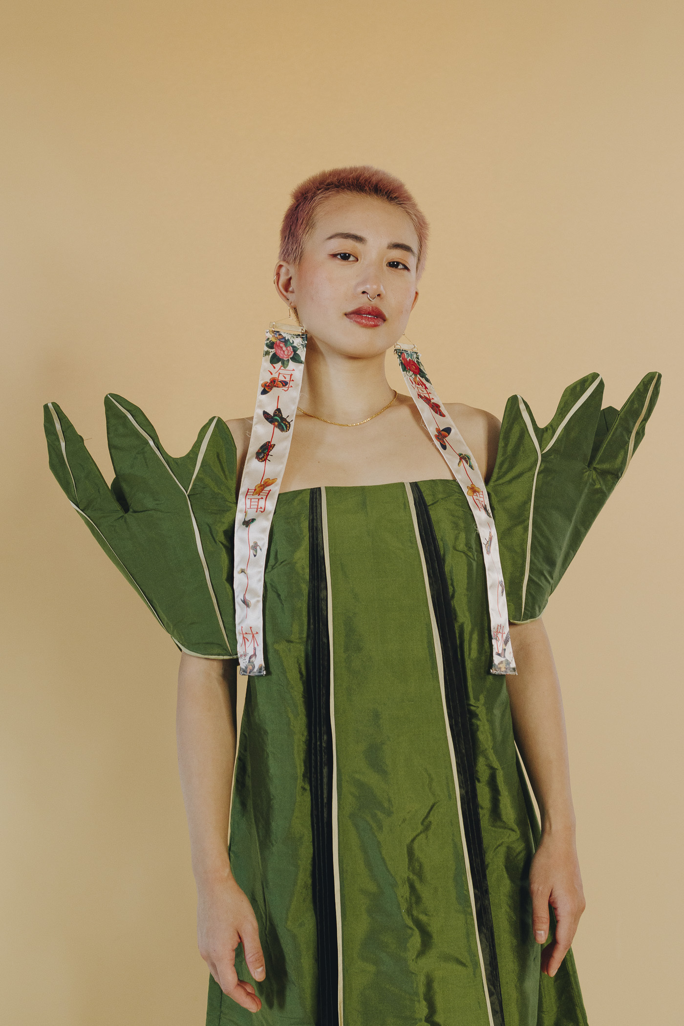 Closer image of Lucky's leaf-inspired dress. Long earring scrolls with butterflies are worn