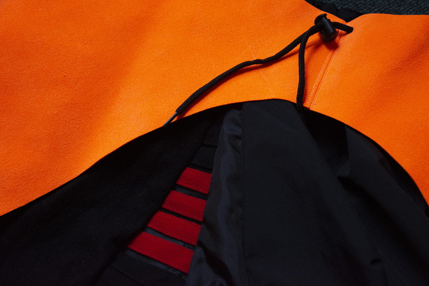 A close-up image of a bright orange fabric that has a black drawstring running through it.