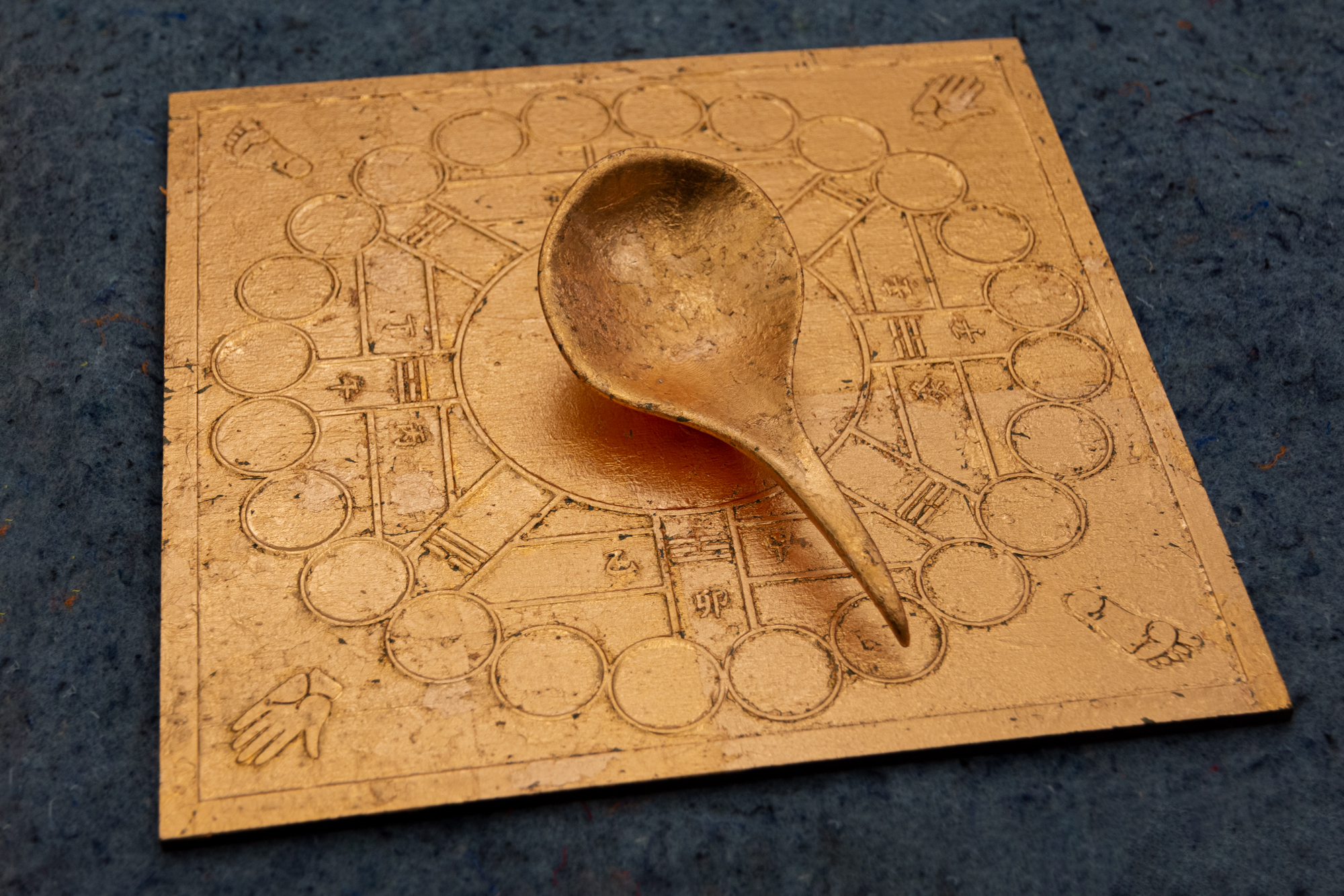 A copper leafed board that simultaneously resembles an early Chinese ladle compass and the spinner from the game of Twister.