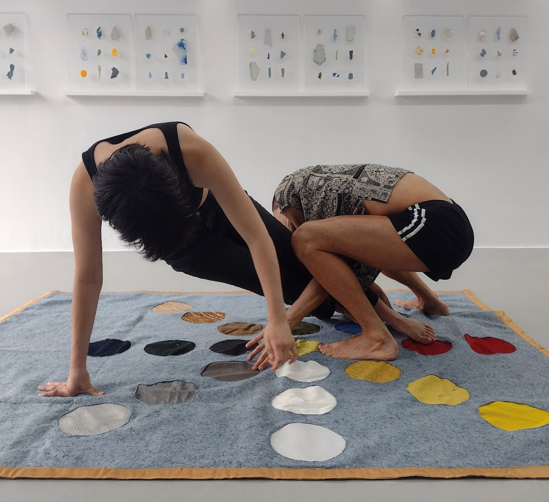 Two bodies appear to be playing the game of twister with their hands and feet on top of a game mat. The mat is designed such that the circles are instead aligned to the 8 cardinal directions rather than a simple array