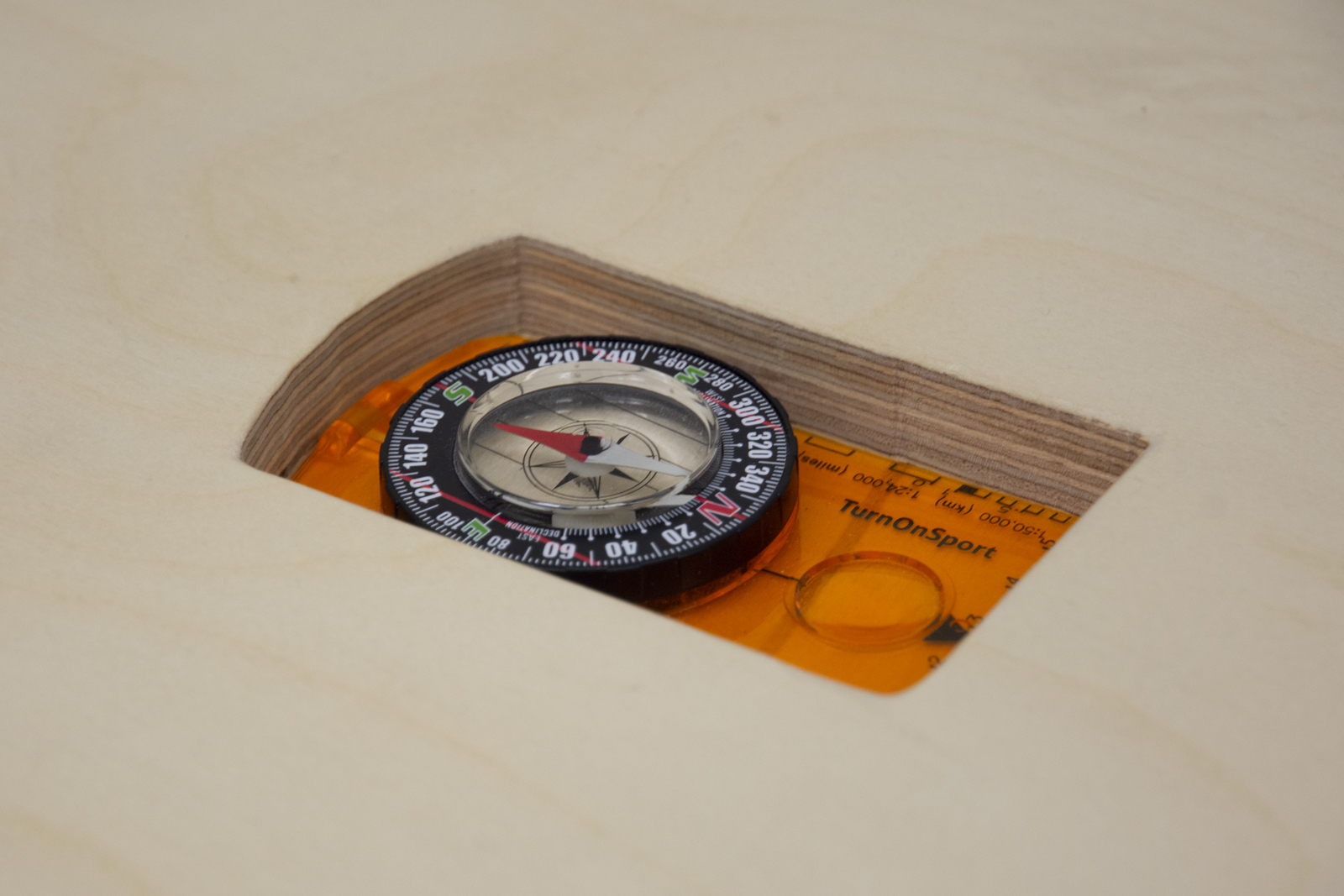 A close-up image of an orange orienteering compass that has been placed within a compartment cut specifically to its size and shape.