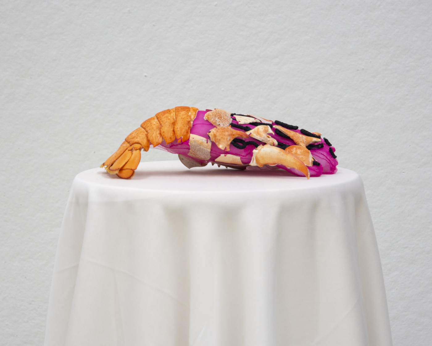 a pink tulle glove covered by lobster shells sits on top of a white fabric draped over a circular surface