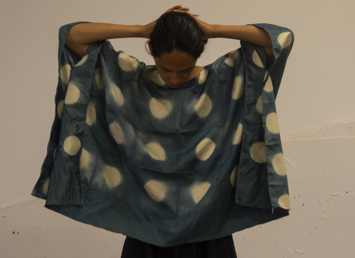 The artist wears a hand-dyed rectangular draped top made using itajime block-resist dyeing techniques.