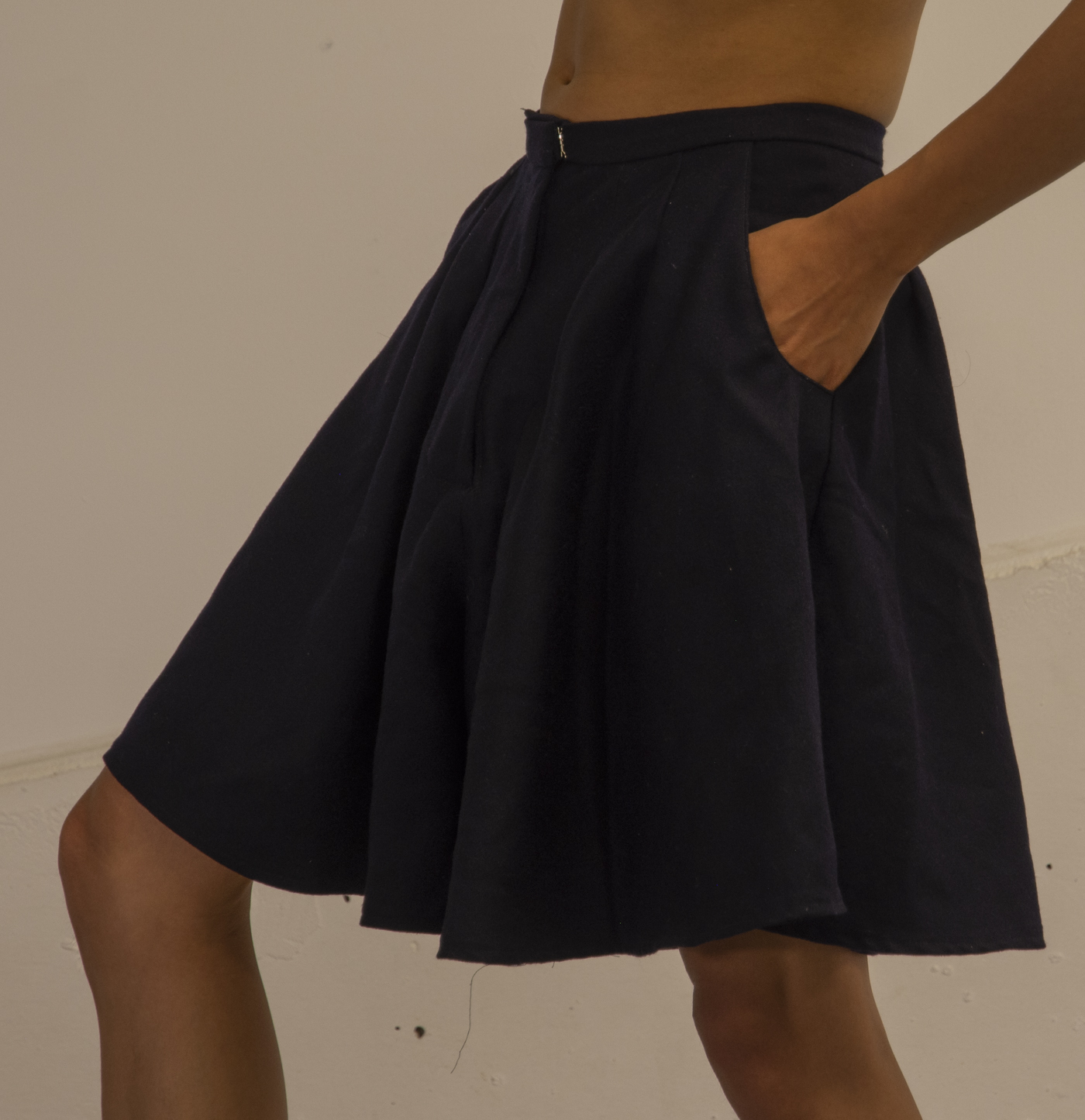 A close-up image of the artist wearing short culottes. Their hand reaches into one of the pockets.