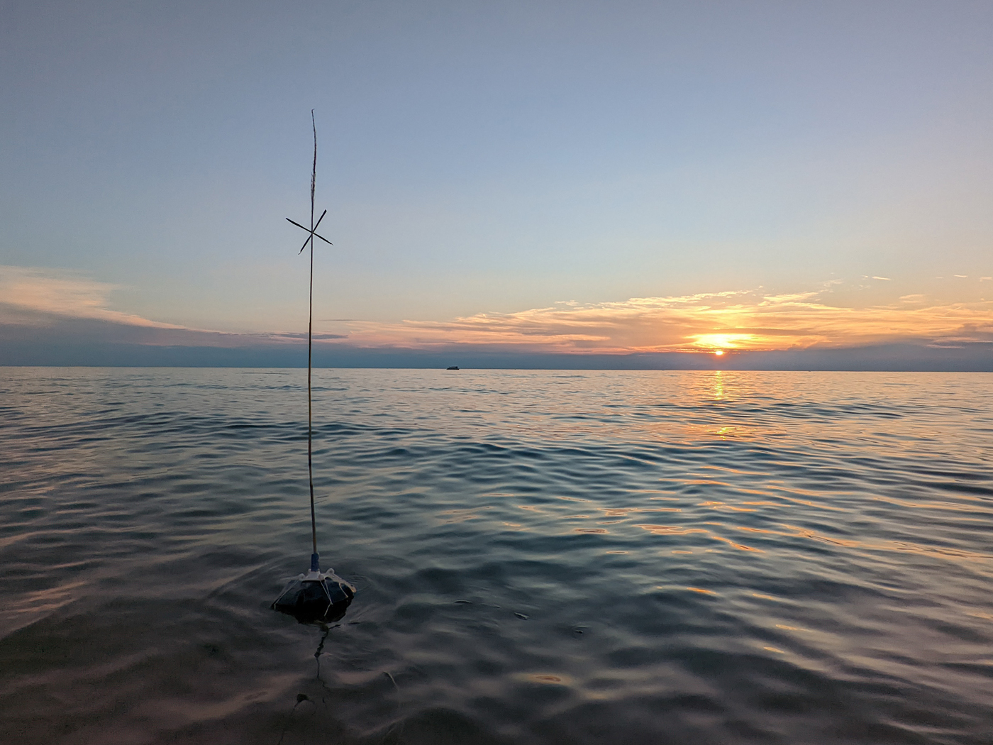 a steel buoy with a reed attached on top of it floats in Lake Michigan at sunset