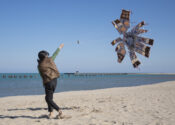 The artist is on a beach flying a kite. The kite does not fly very well.