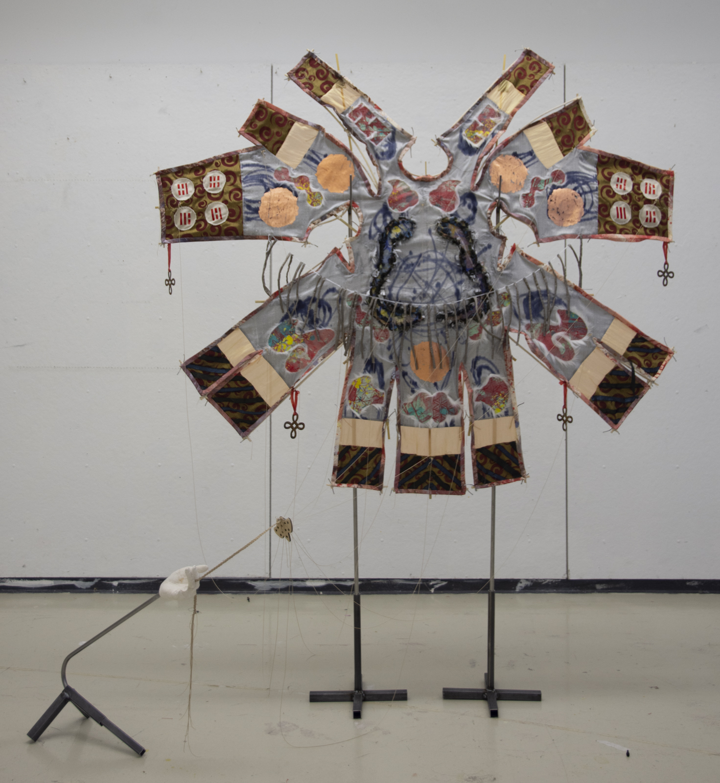 A ceremonial looking kite is held up with two metal poles. A plaster hand holds the kiteline.