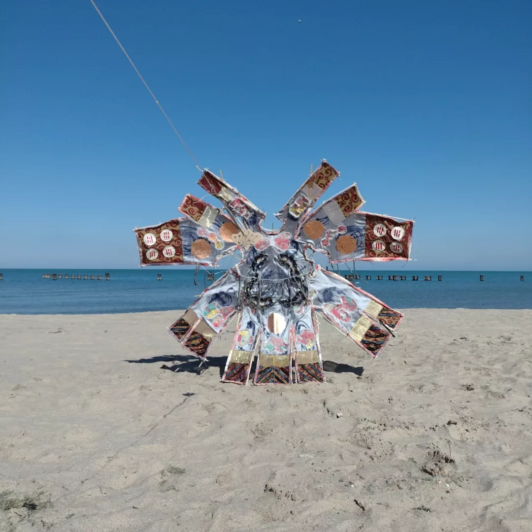 The kite is balanced such that it is standing up on the beach sand without falling over.