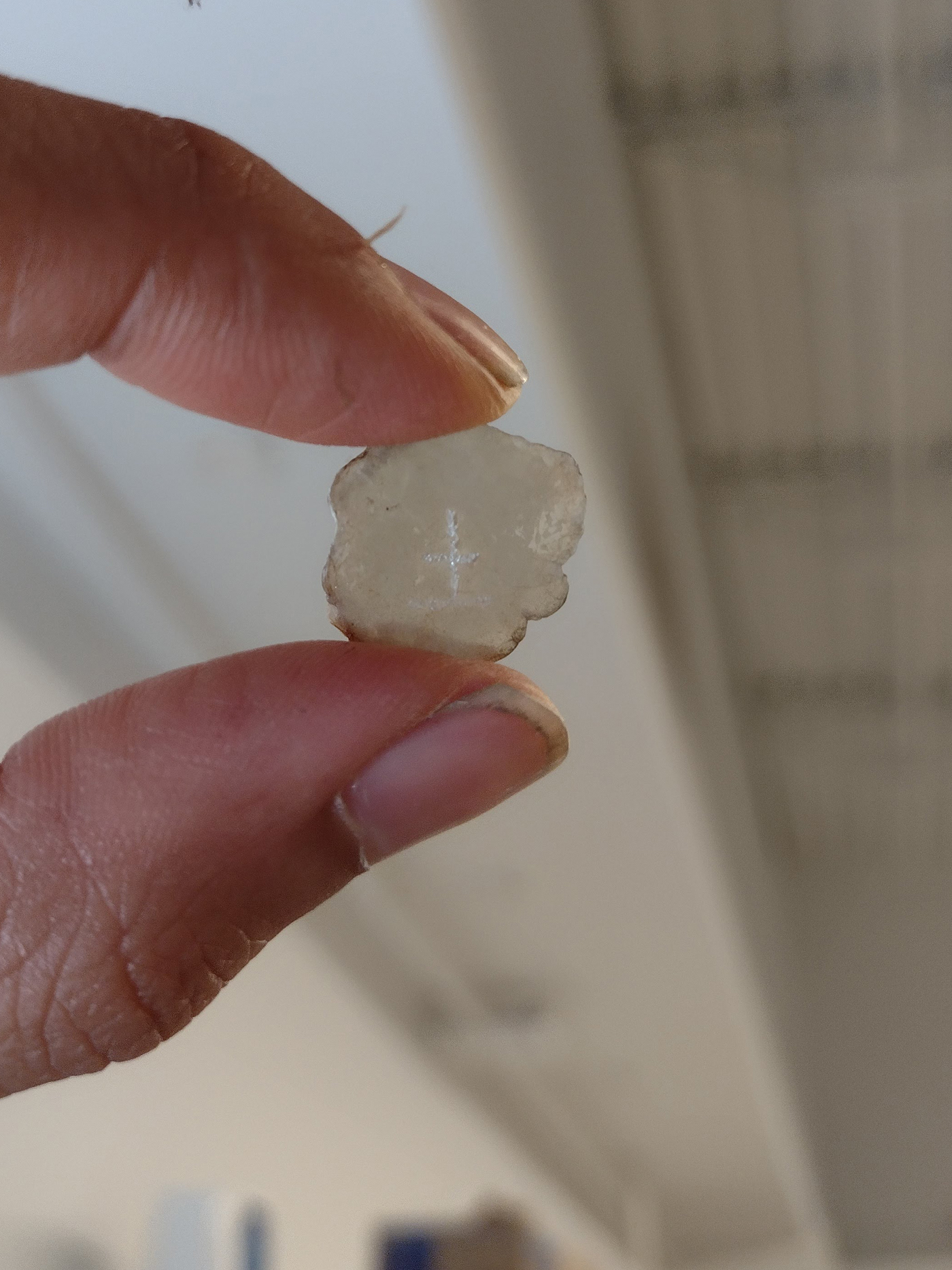 two fingers hold up a piece of mica that has a chinese character for "earth" etched into it.