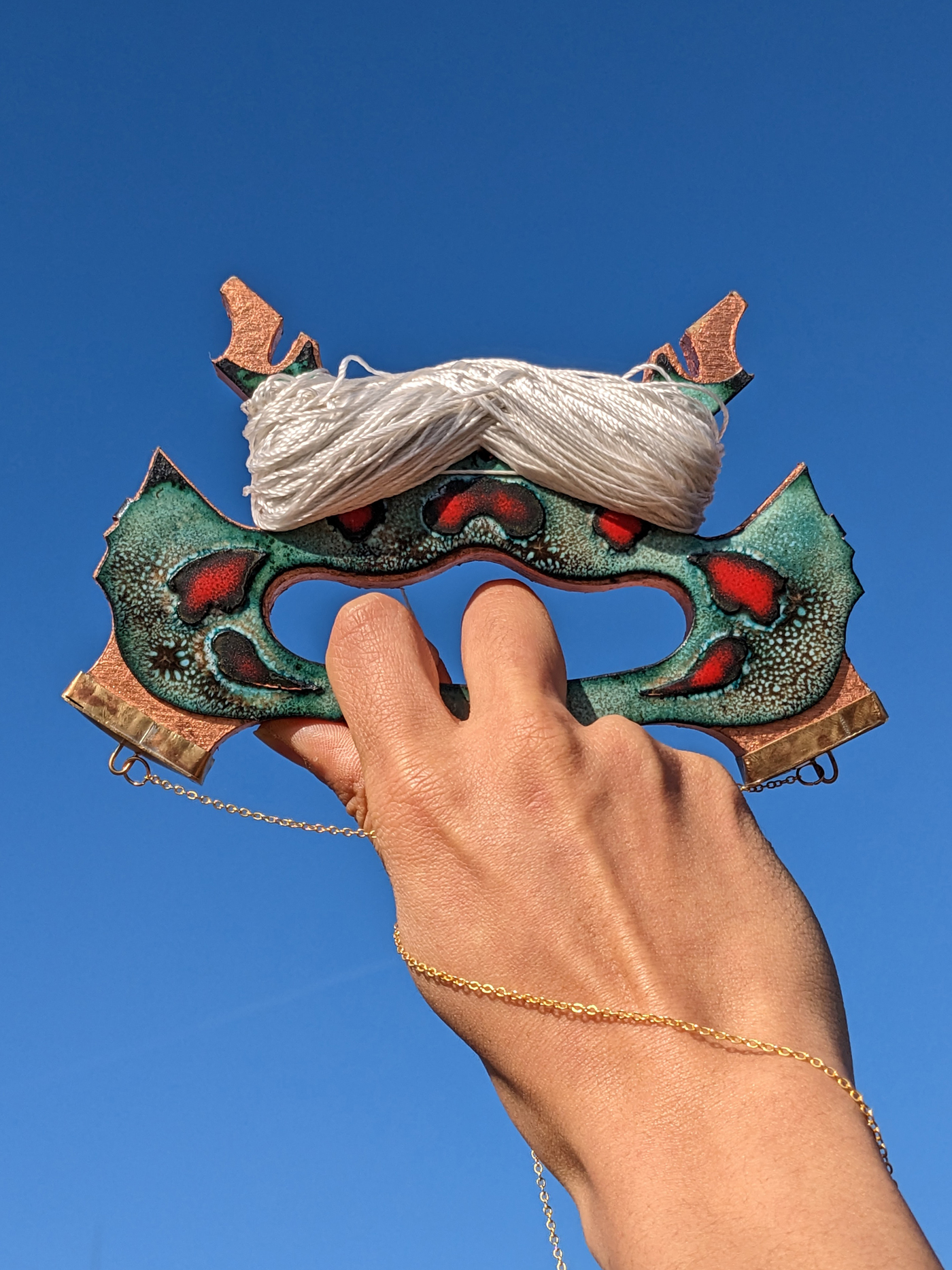 a hand holding a kite reel made of copper leafed wood with an enameled copper plate